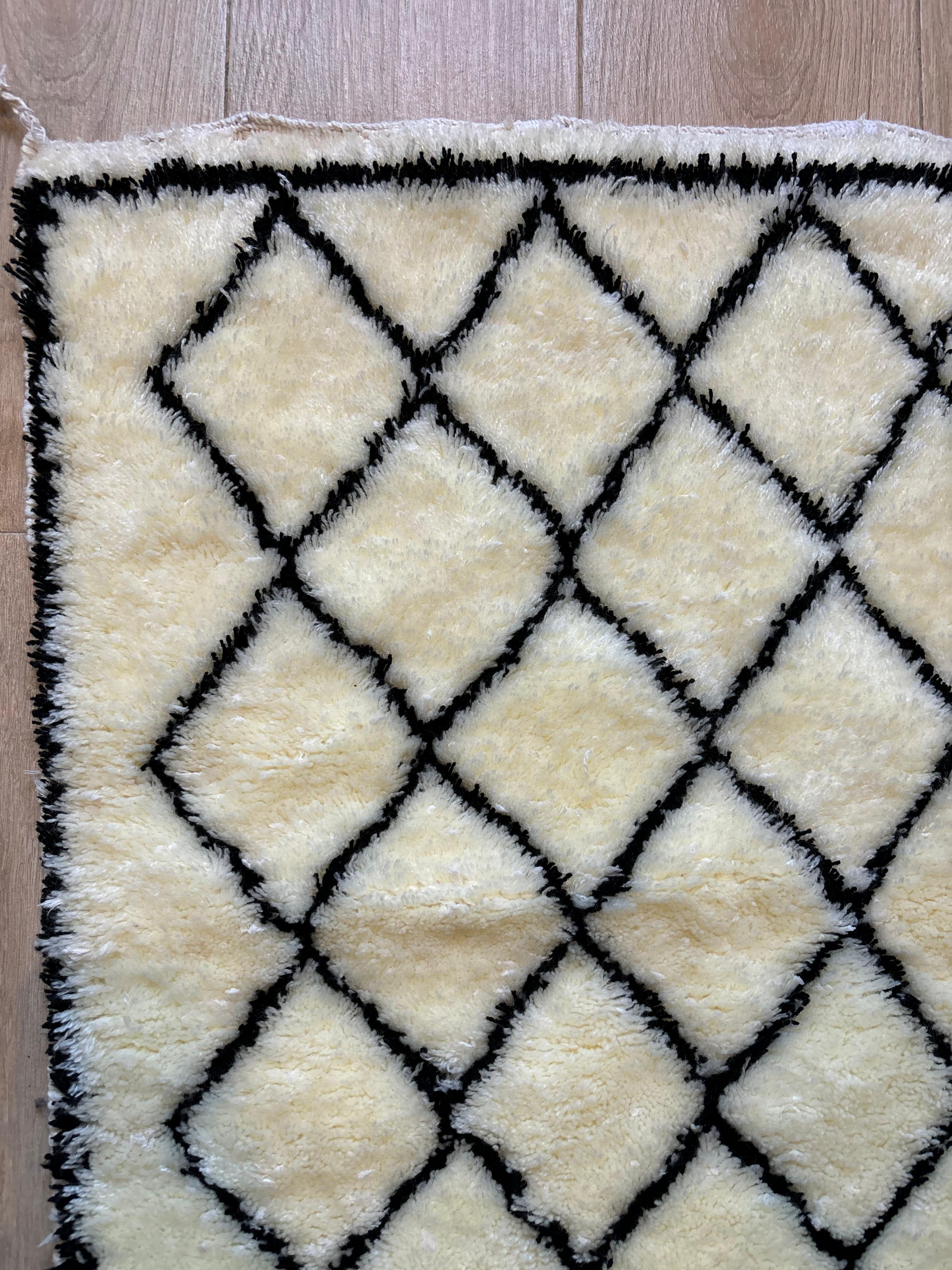 Close-up of corner on Beni Ourain Moroccan rug with cream wool and black diamond pattern on wooden floor