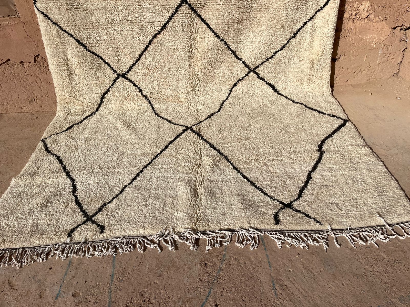 Handwoven Moroccan rug with black diamond pattern on cream wool, styled outdoors