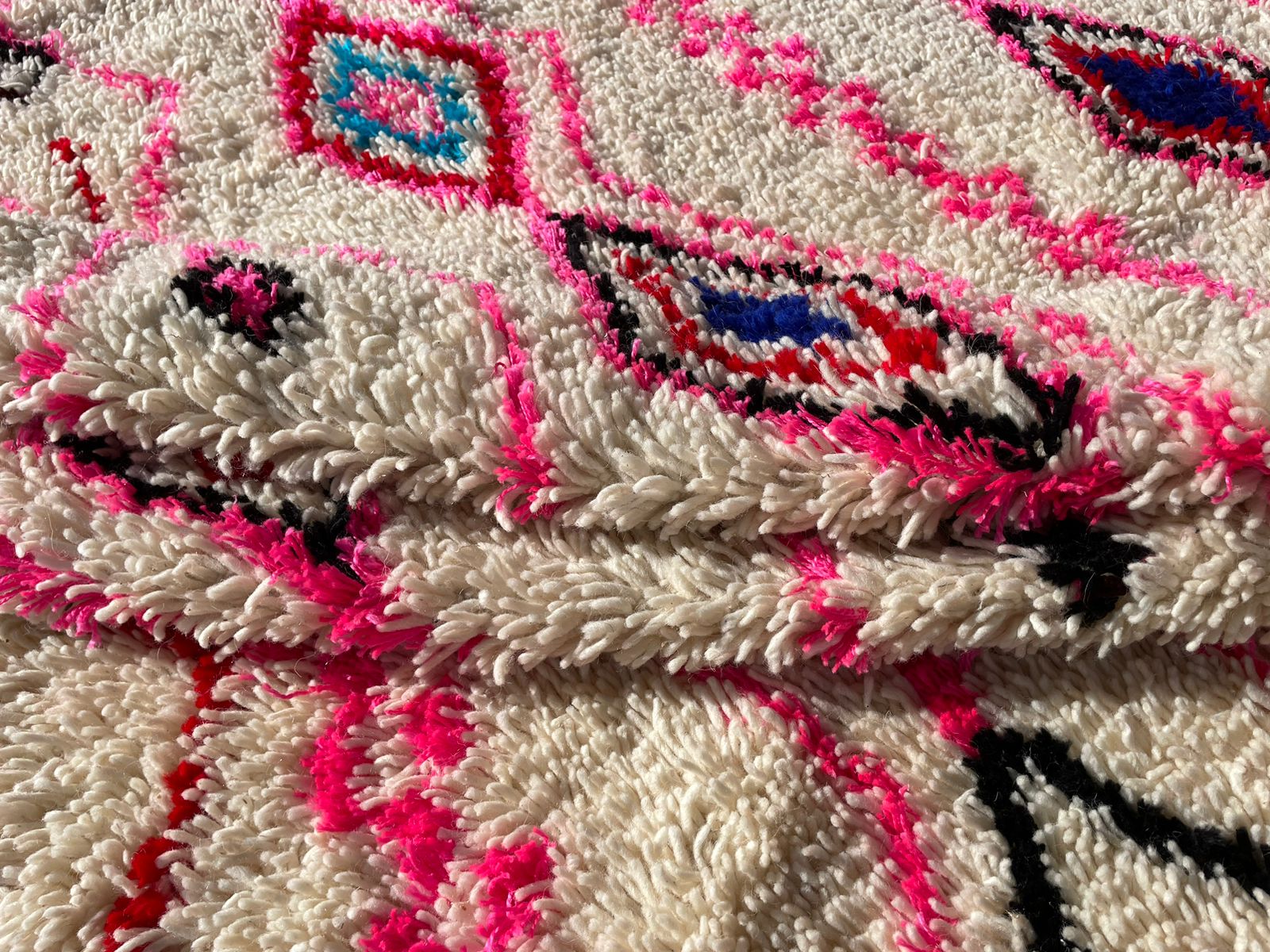 Close-up of Moroccan boho rug showing pink, blue, and black diamond texture on wool surface