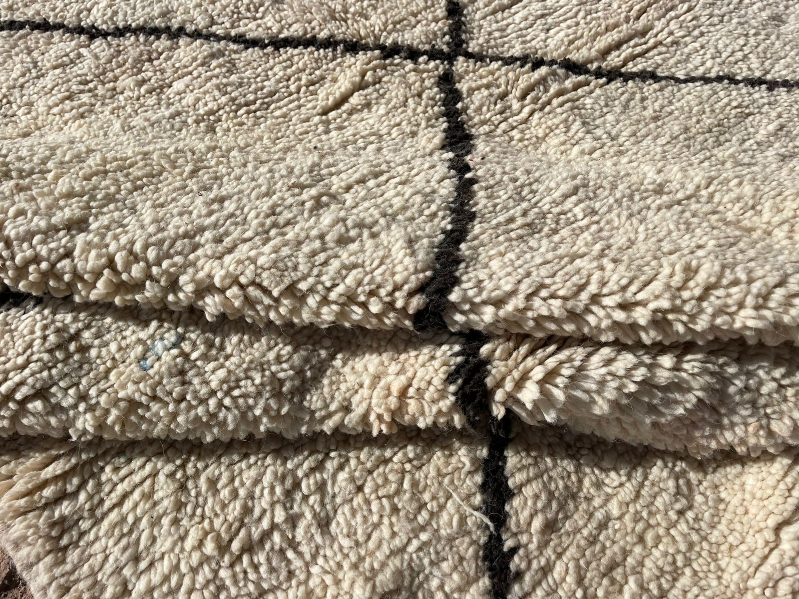 Close-up of a soft wool Moroccan rug with black line detailing and thick texture