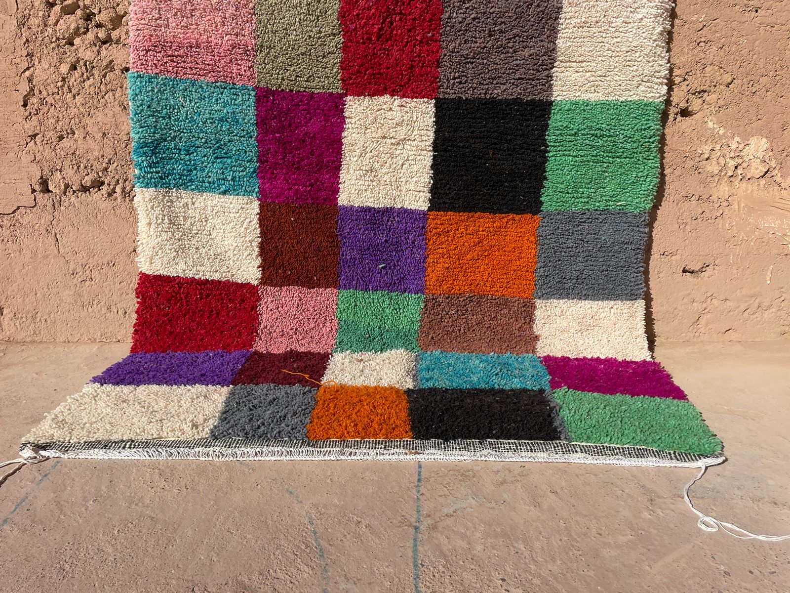 Handmade Moroccan shag rug with multicolor checkered wool pattern, displayed against a clay wall, 5x8 feet