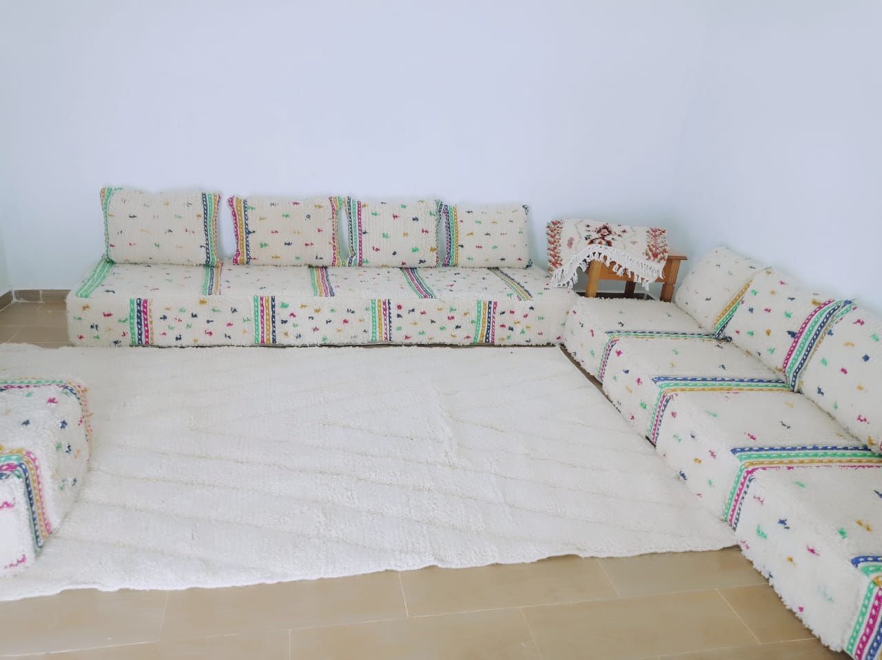 Spacious Moroccan floor sofa set with colorful Berber accents and a large ivory handmade wool rug for cozy living spaces.