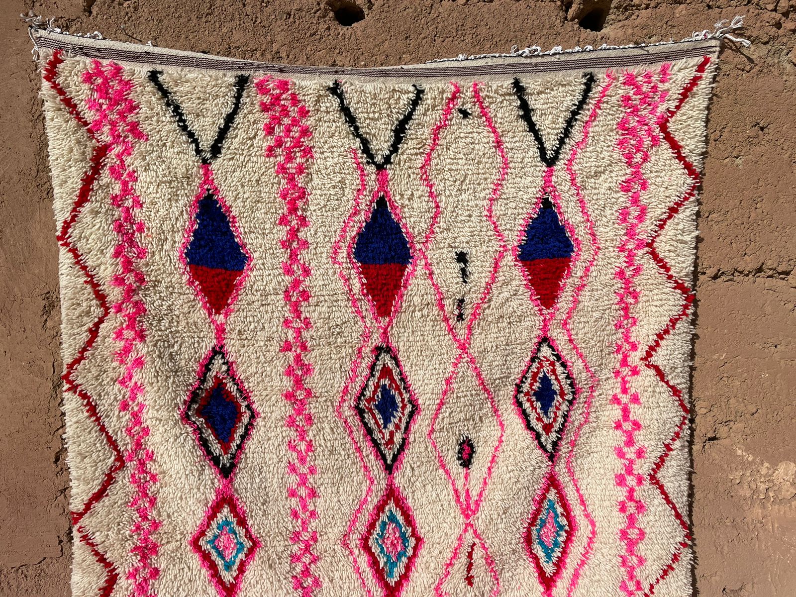 Handmade Moroccan Berber rug in pink and blue with boho tribal motifs hanging on a rustic wall