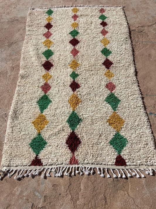 Outdoor photo of handmade Moroccan boho wool rug with green, mustard, red, and pink diamond patterns on a beige base, 5x8 feet