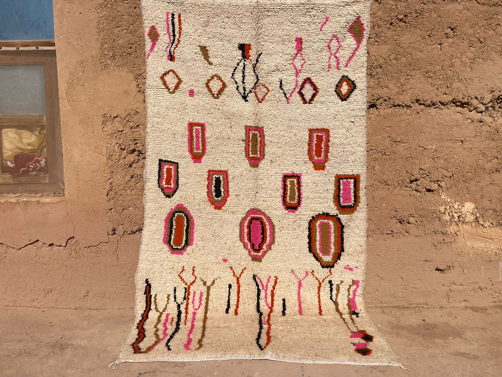 Outdoor view of handmade Moroccan boho wool rug with abstract pink, orange, and black shapes on a beige background, 5x8 feet