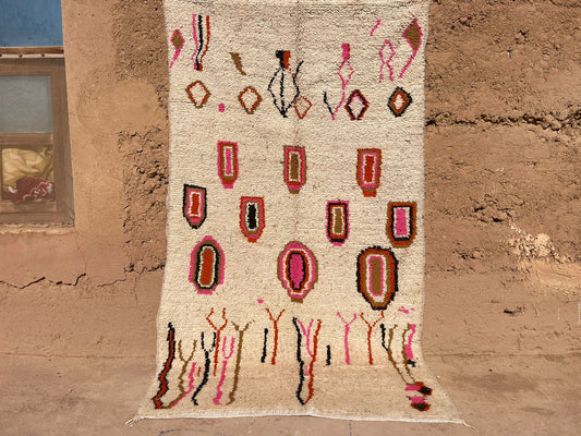 Outdoor view of handmade Moroccan boho wool rug with abstract pink, orange, and black shapes on a beige background, 5x8 feet