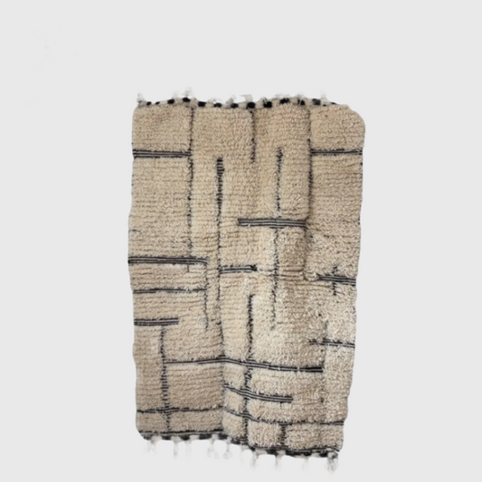 Flat lay of handmade Moroccan rug in cream with black geometric lines, wool material