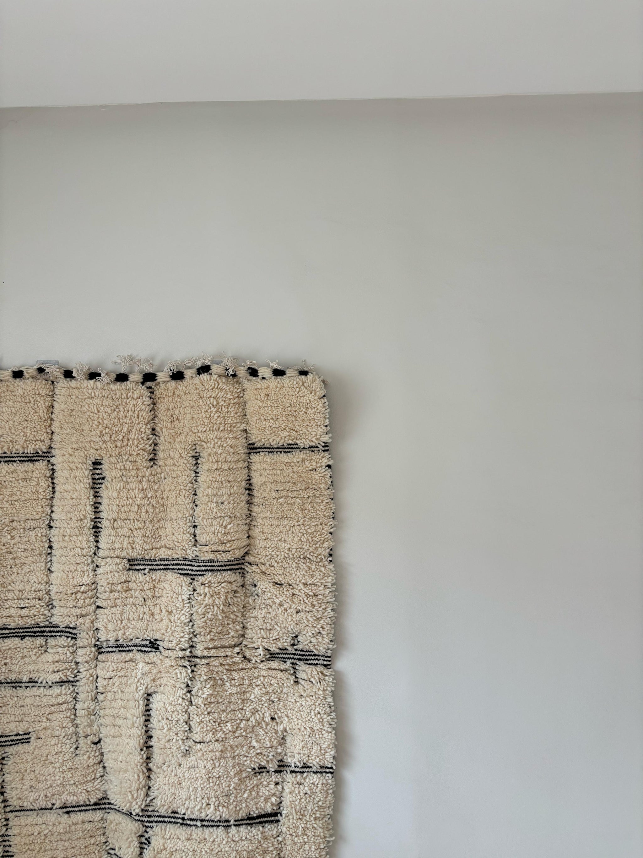 Modern Moroccan wool rug with cream base and black geometric lines, styled as wall hanging