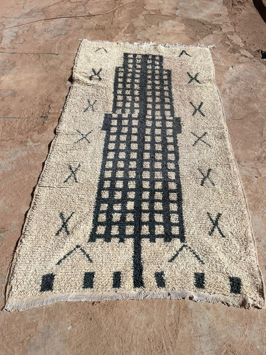 Outdoor view of handmade Moroccan wool rug in beige with bold black grid pattern and tribal X motifs, 5x8 feet