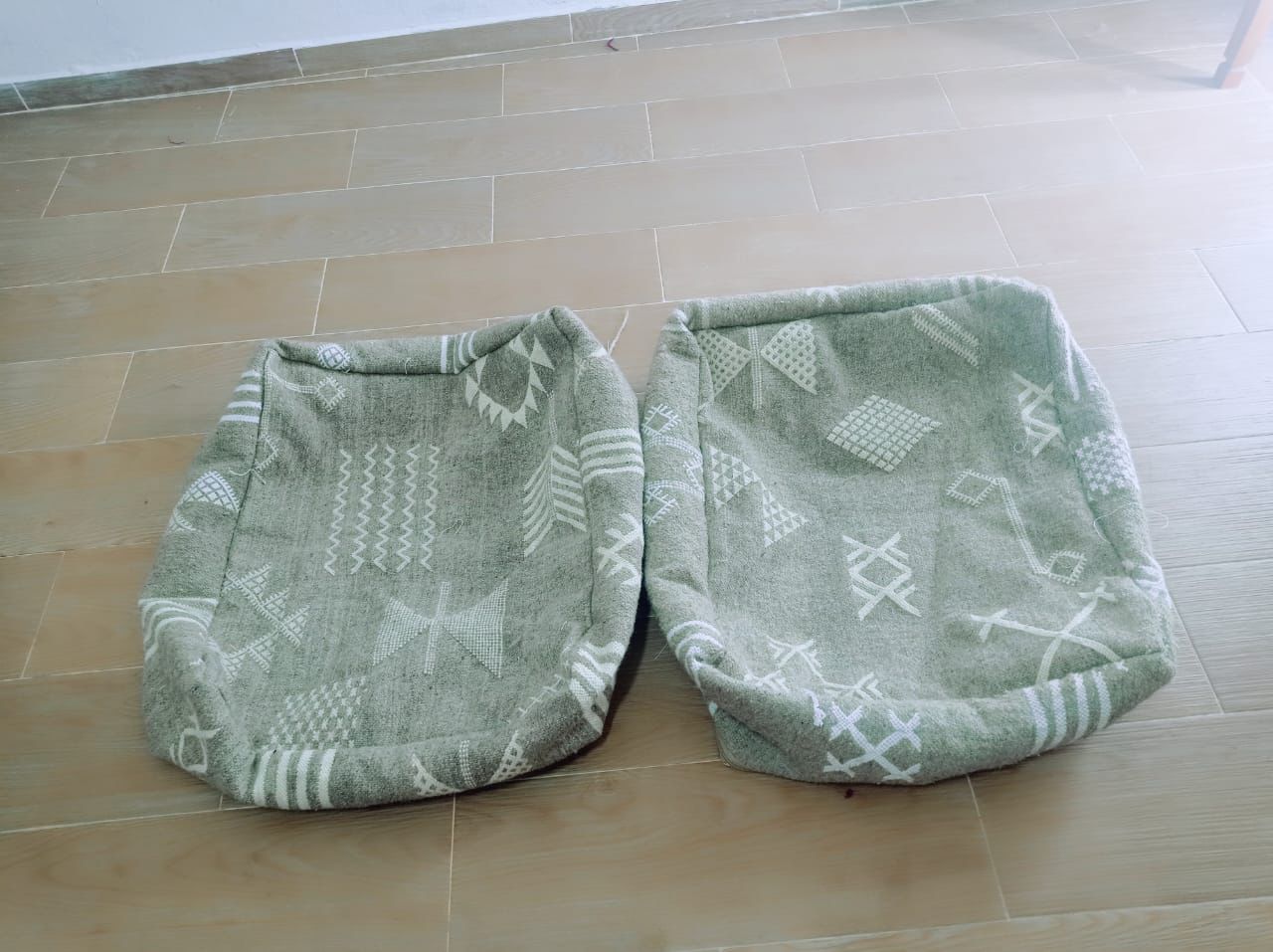 Pair of handmade Moroccan pouf covers in grey with white tribal patterns, shown on wooden floor from top view