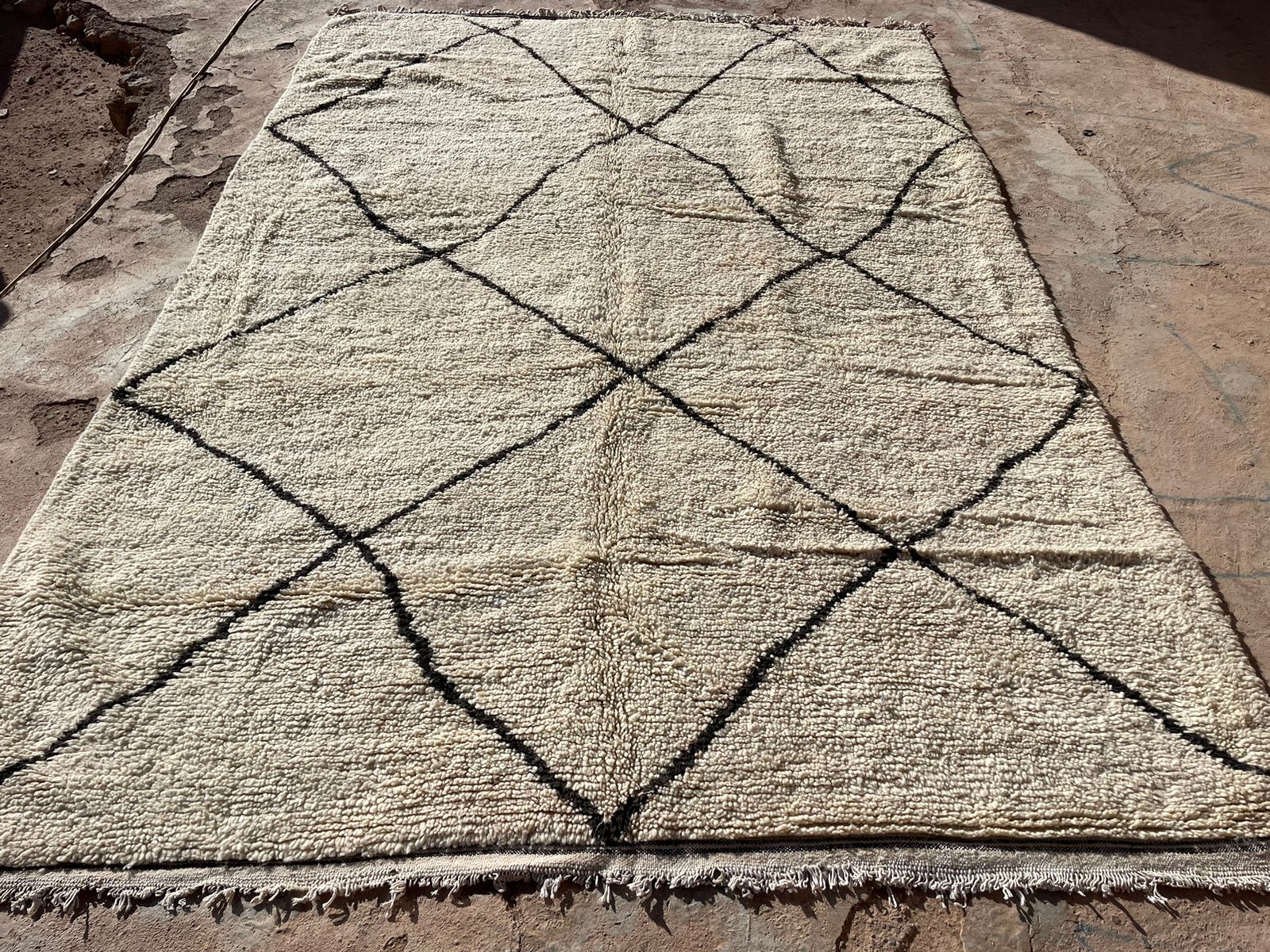 Flat view of a Moroccan wool rug with black diamond pattern on neutral background