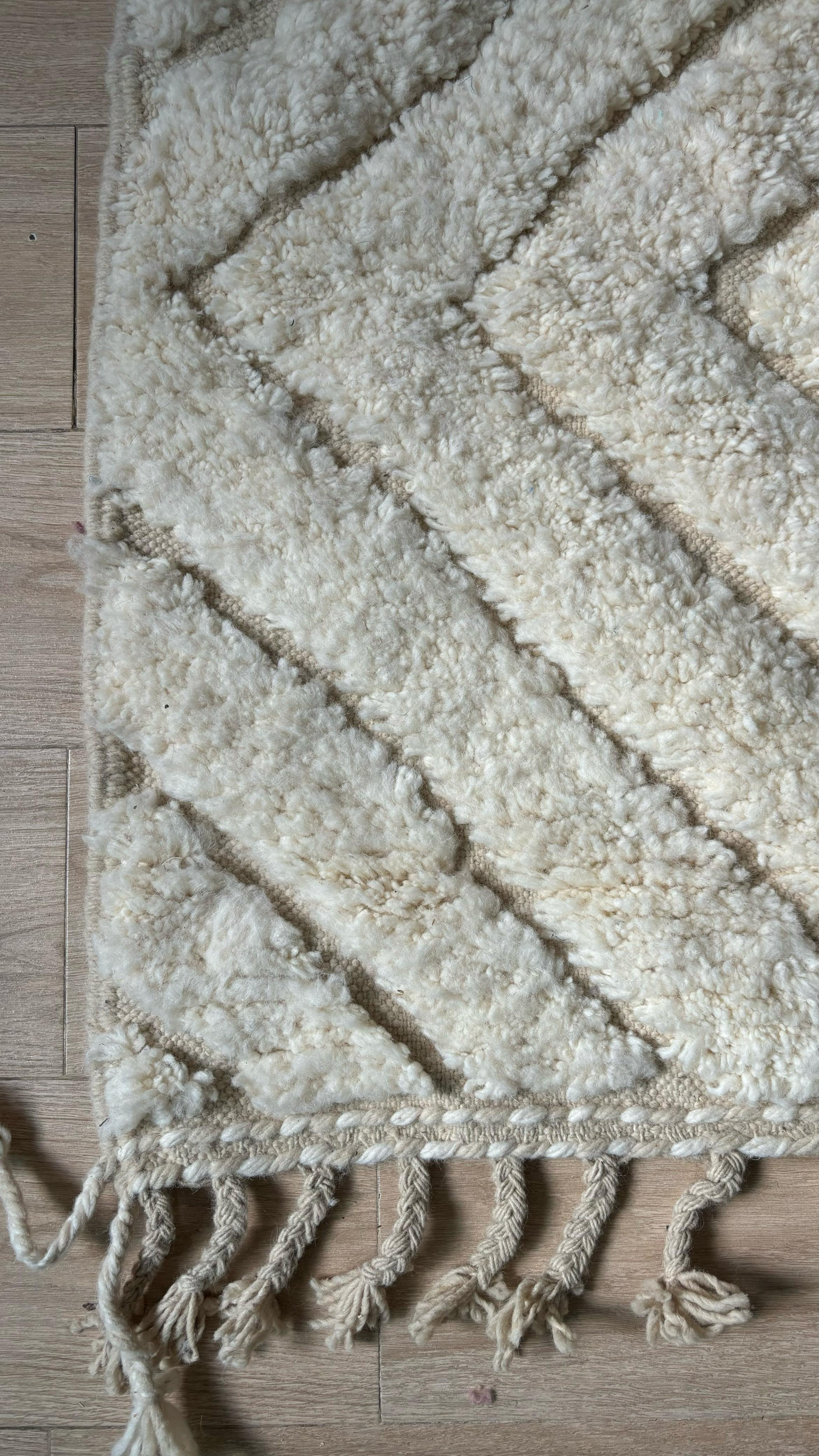 Corner of cream Moroccan wool rug with chevron pattern and knotted fringe, close-up view