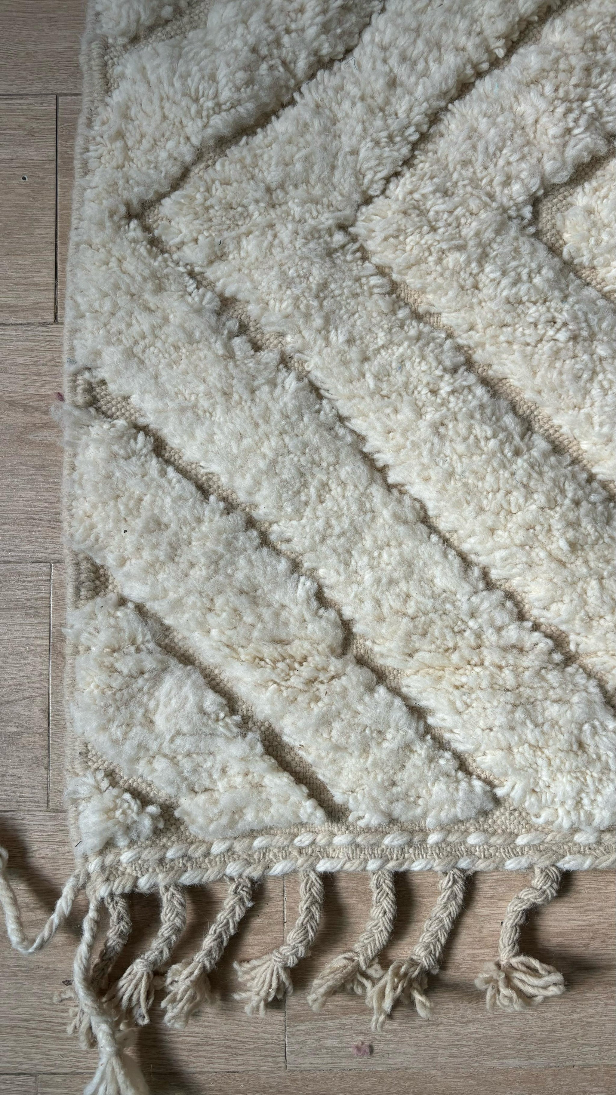Corner of cream Moroccan wool rug with chevron pattern and knotted fringe, close-up view