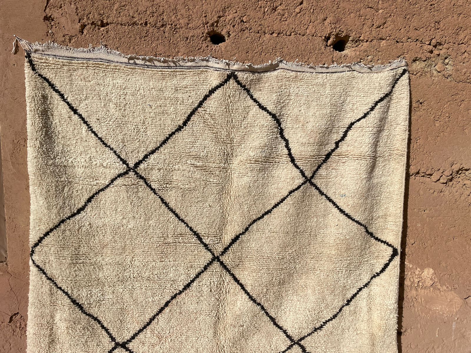 Hanging Moroccan Berber rug with black crisscross lines on beige wool