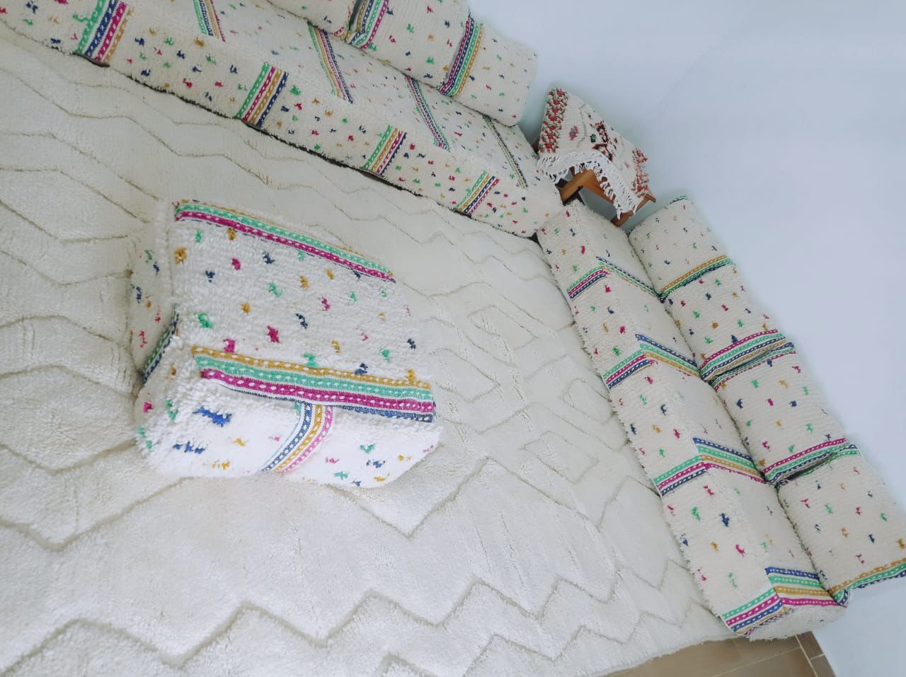 Handmade Moroccan sofa set with colorful embroidered pillows and a large ivory wool rug featuring a subtle chevron pattern.