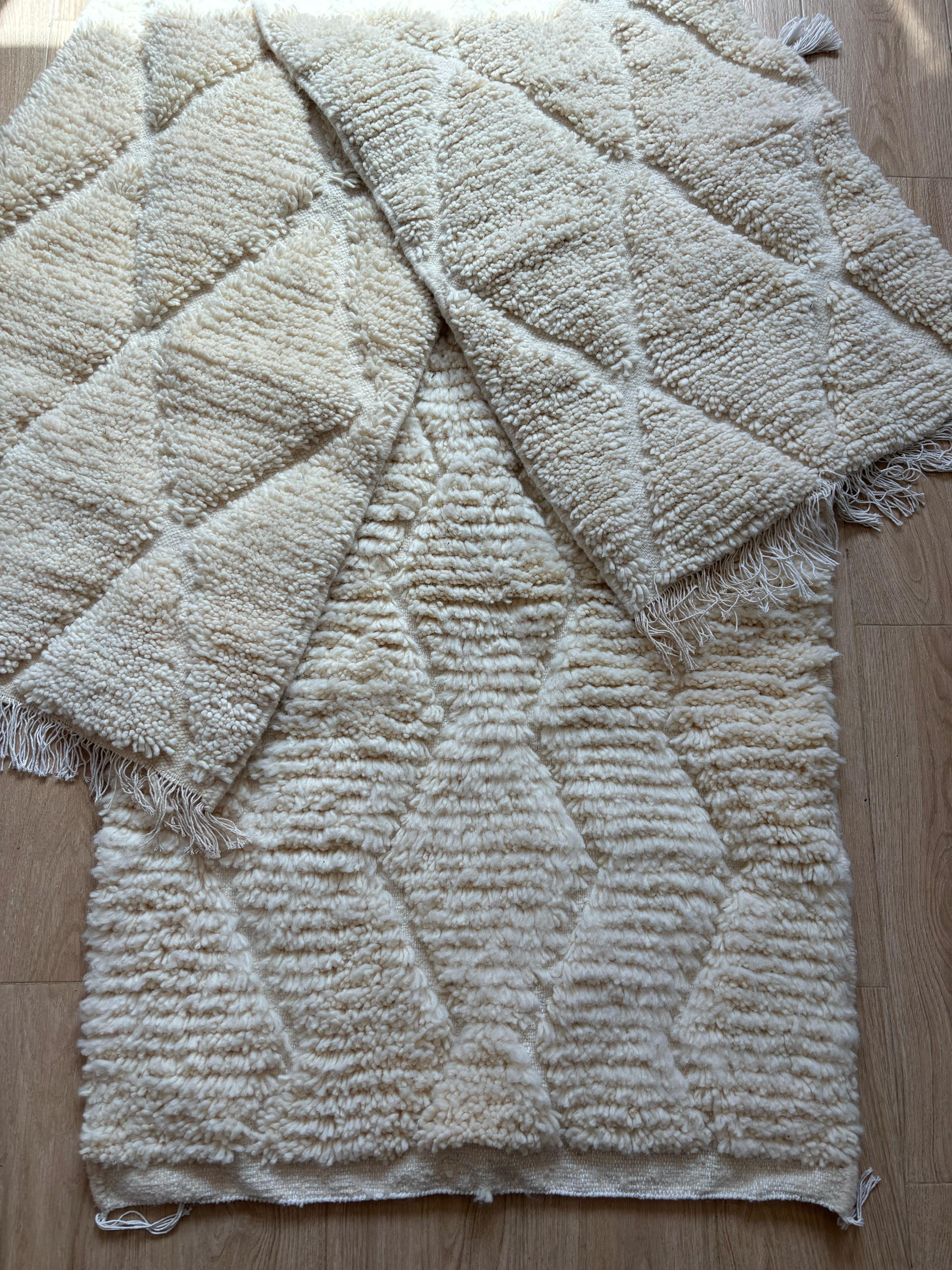 Layered Moroccan wool rugs in cream with thick textured diamond pattern, styled on wood floor
